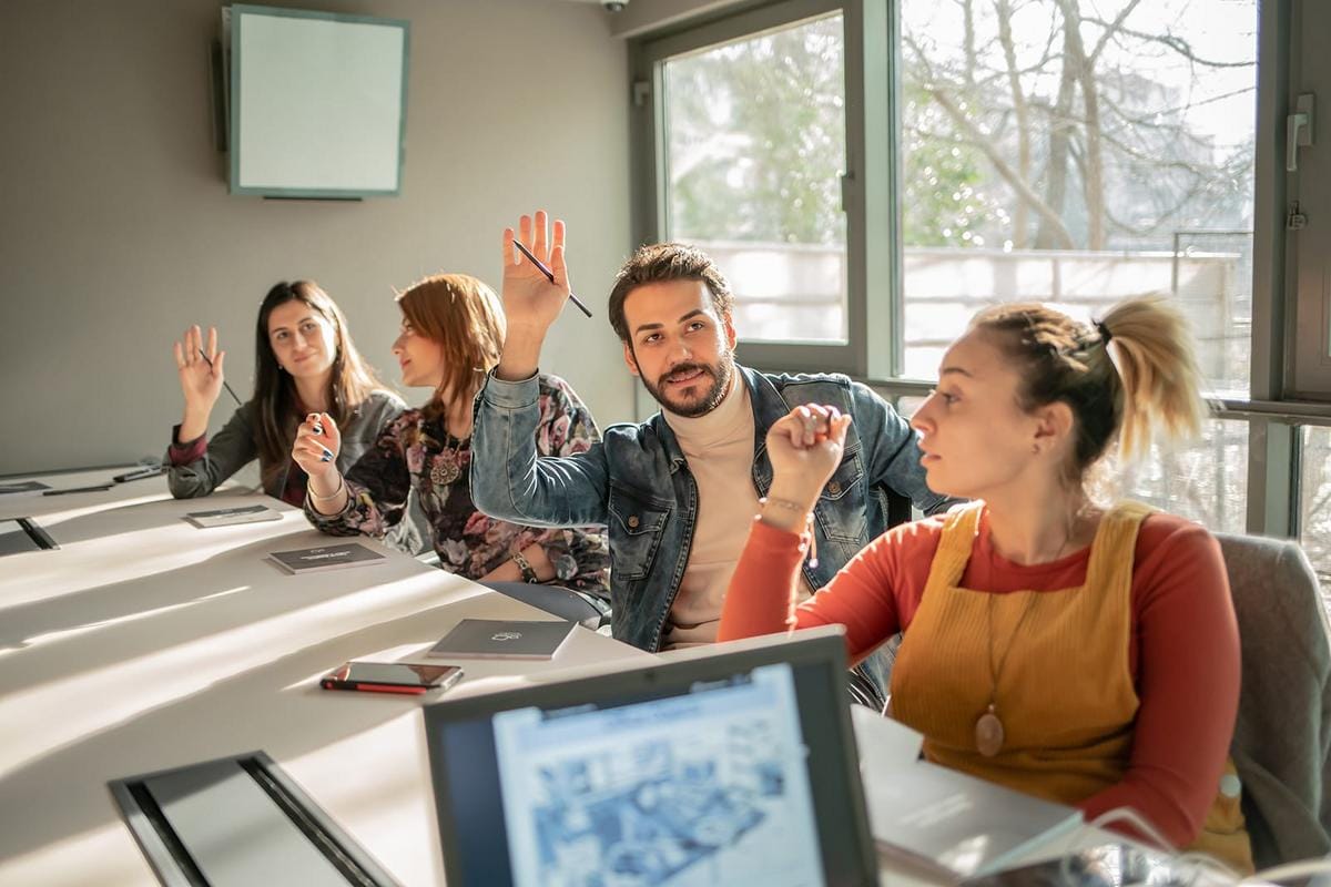 An engaging image of a teacher leading a small group of adult students in a lively conversation session, in a cozy classroom setting, with online platform interface visible on screen, emphasizing personalized attention and interaction