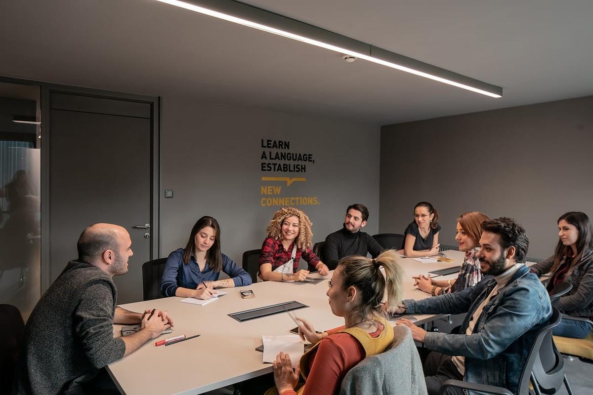 A high-resolution image showing a diverse group of adult students participating in an interactive English speaking class, with teachers guiding and students practicing conversations in a modern classroom environment, both online and physical classroom settings, vibrant and engaging atmosphere
